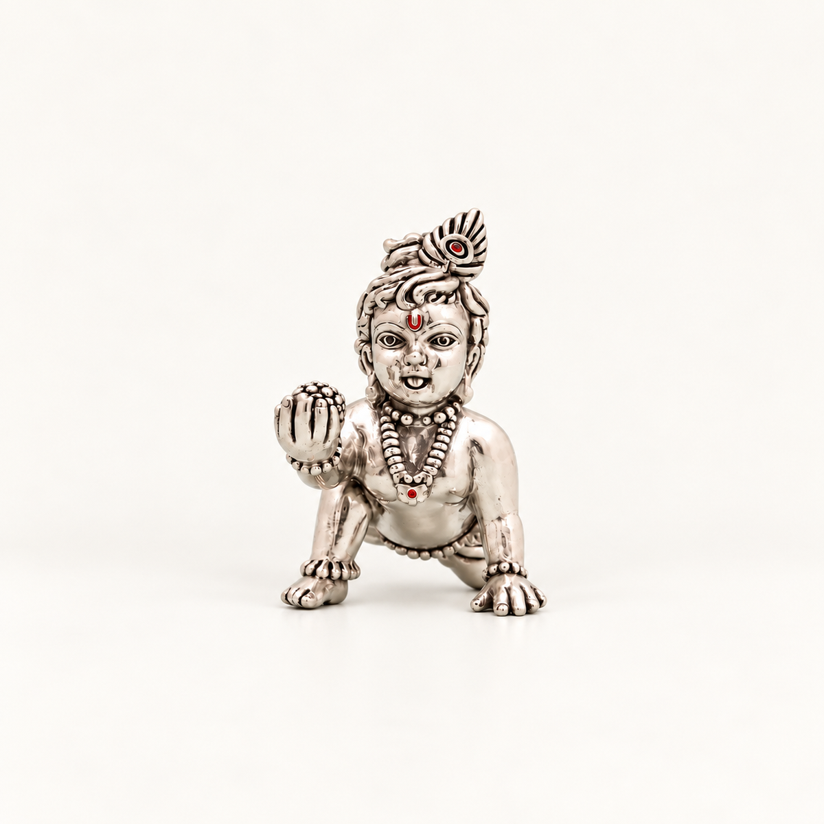 Front view of a silver crawling Laddu Gopal idol holding a sweet against an off-white background.