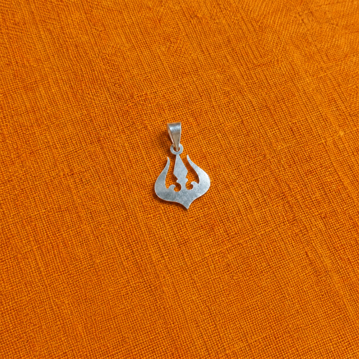 925 silver trishul pendant with a symmetrical cutout design on orange fabric