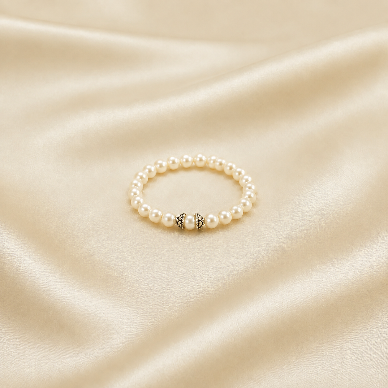 A pearl beaded stretch bracelet with a central silver-toned decorative bead, displayed on a draped cream satin fabric background.