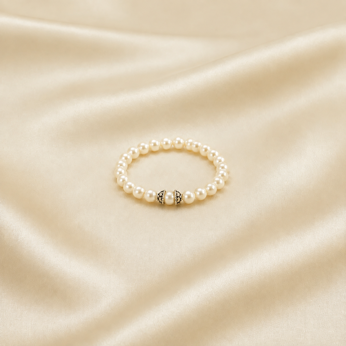 A pearl beaded stretch bracelet with a central silver-toned decorative bead, displayed on a draped cream satin fabric background.