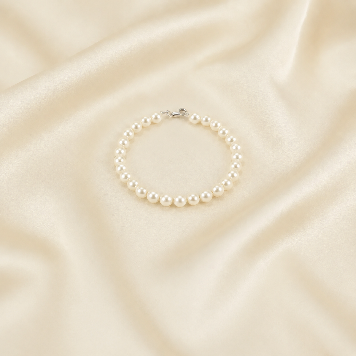 A classic pearl bracelet with a silver clasp, displayed on a draped cream satin fabric background.