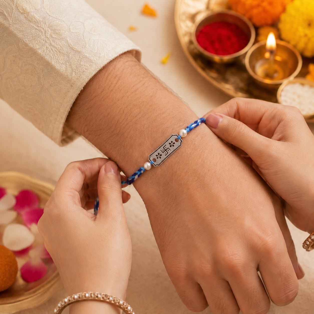 Hands tying 925 pure silver Swastik floral engraved pearl rakhi bracelet on blue cord on brother wrist for Raksha Bandhan