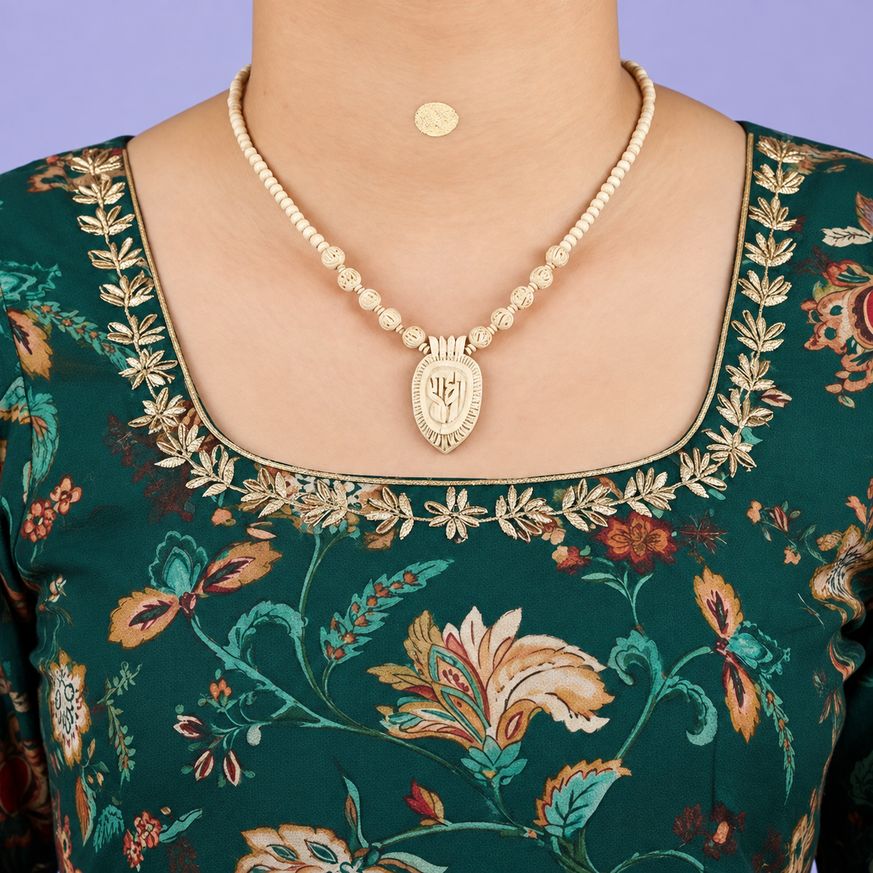 Handcrafted wooden bead necklace with carved Radha pendant worn with a dark green floral embroidered traditional outfit