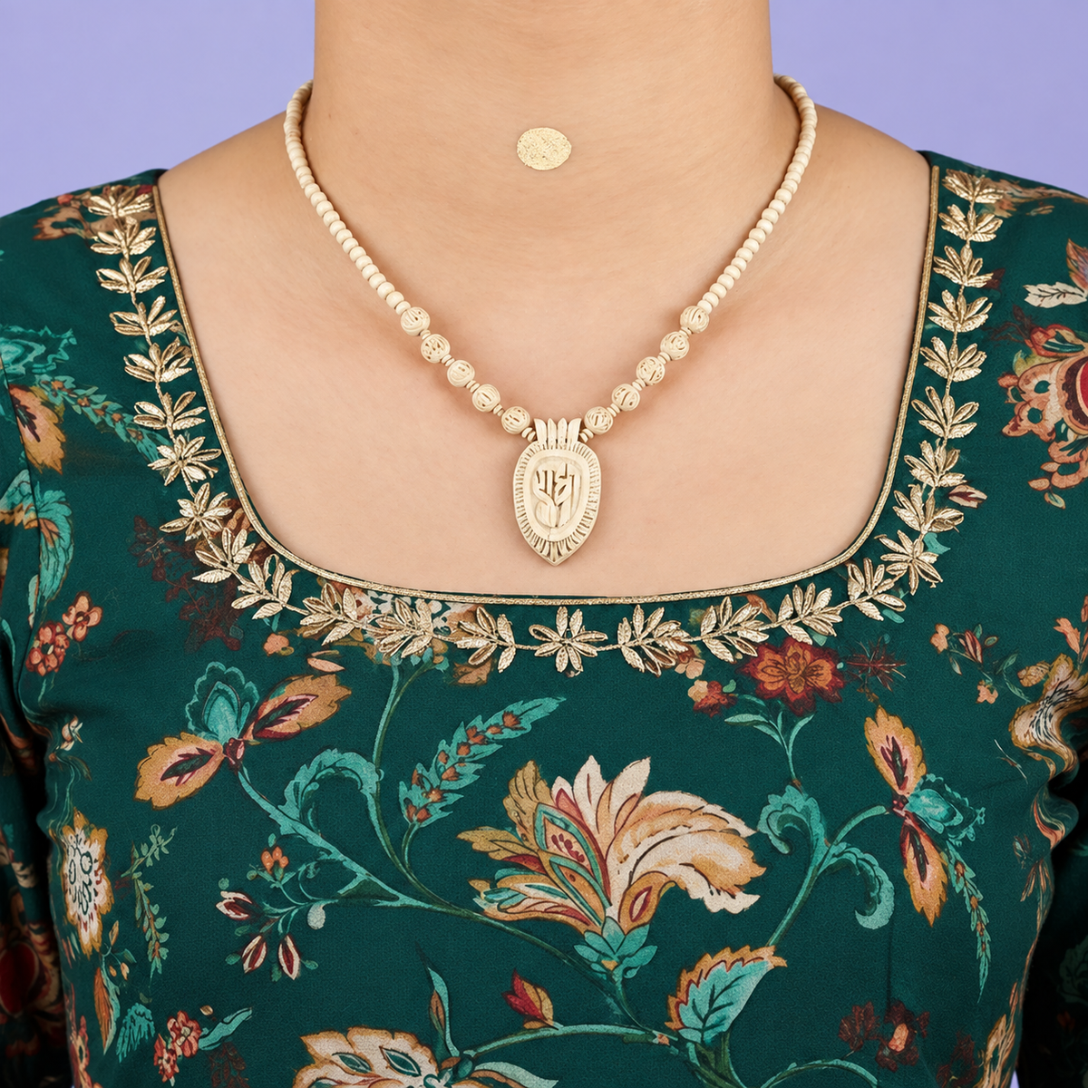 Handcrafted wooden bead necklace with carved Radha pendant worn with a dark green floral embroidered traditional outfit