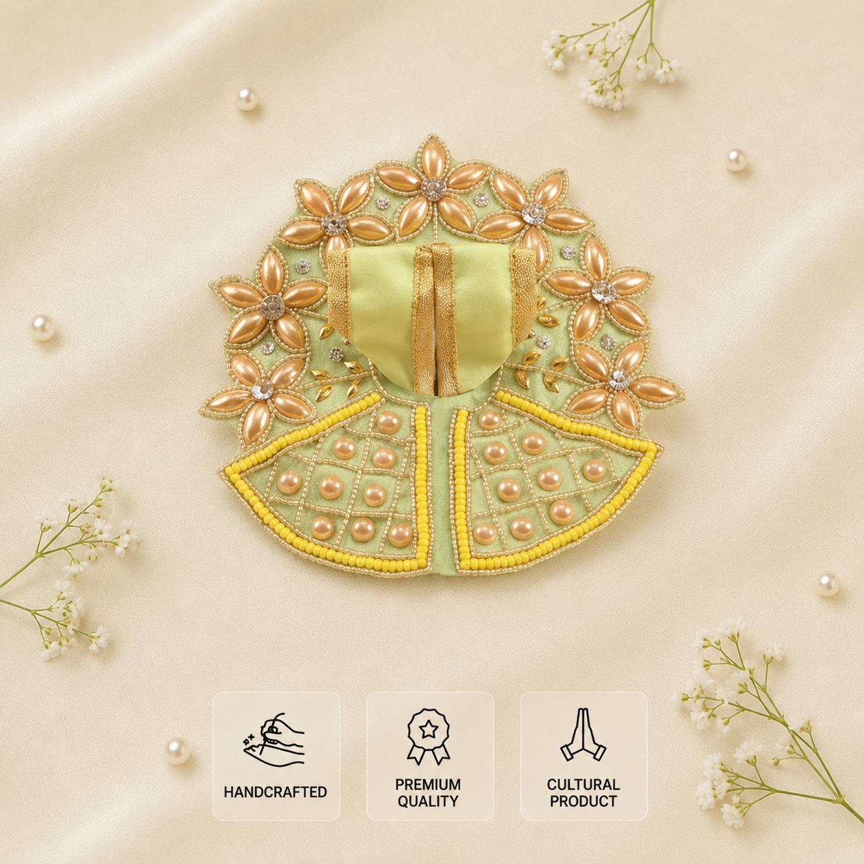 A decorative embroidered poshak or dress laid flat on a soft beige satin background, surrounded by small white flowers and pearl-like beads. The item has a pale yellow-green base with metallic gold floral embroidery, yellow trim, and pearl embellishments.