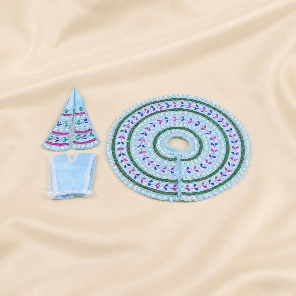 A light blue embroidered with green and purple accents, shown with two matching small ornaments and a folded matching fabric piece on a beige satin background.
