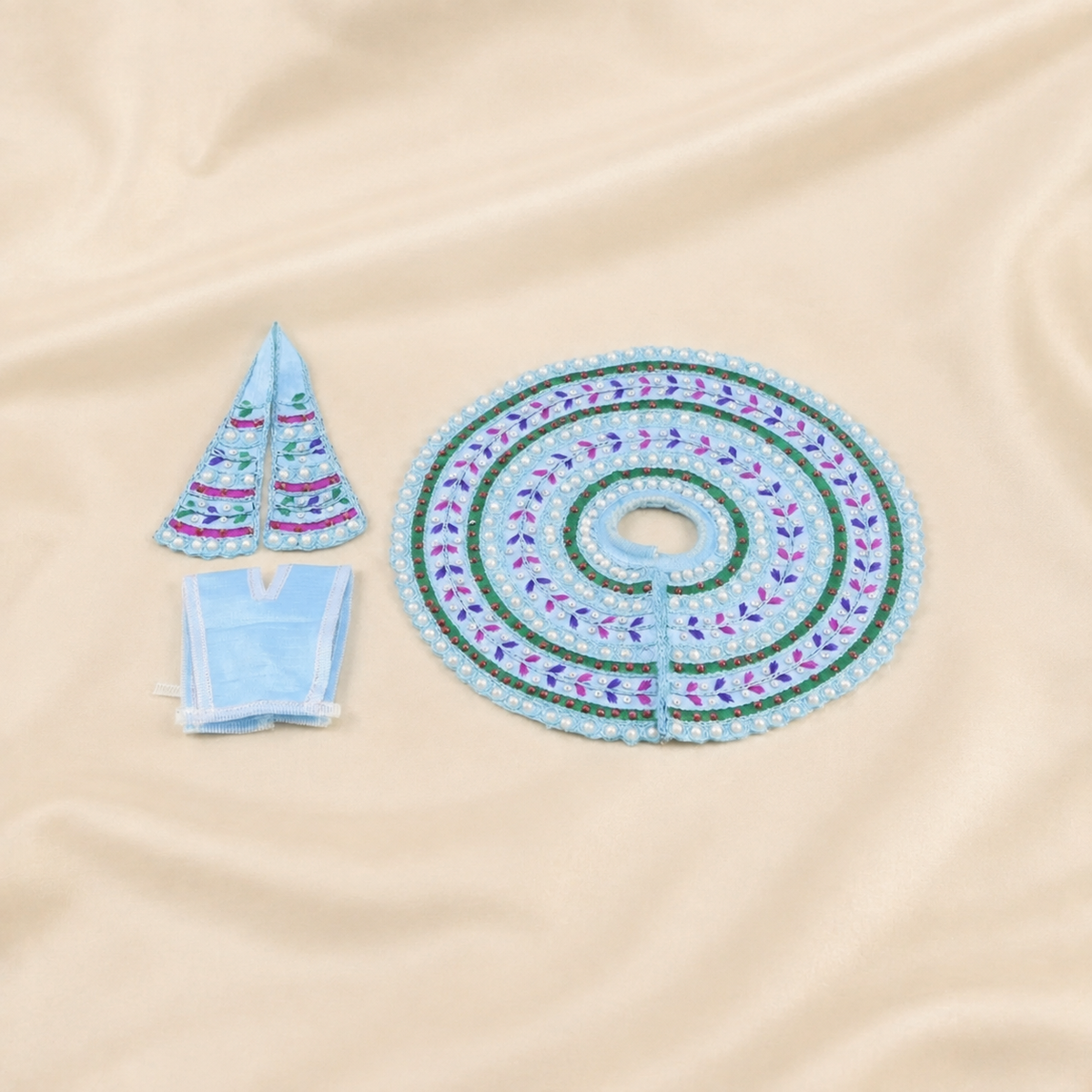 A light blue embroidered with green and purple accents, shown with two matching small ornaments and a folded matching fabric piece on a beige satin background.