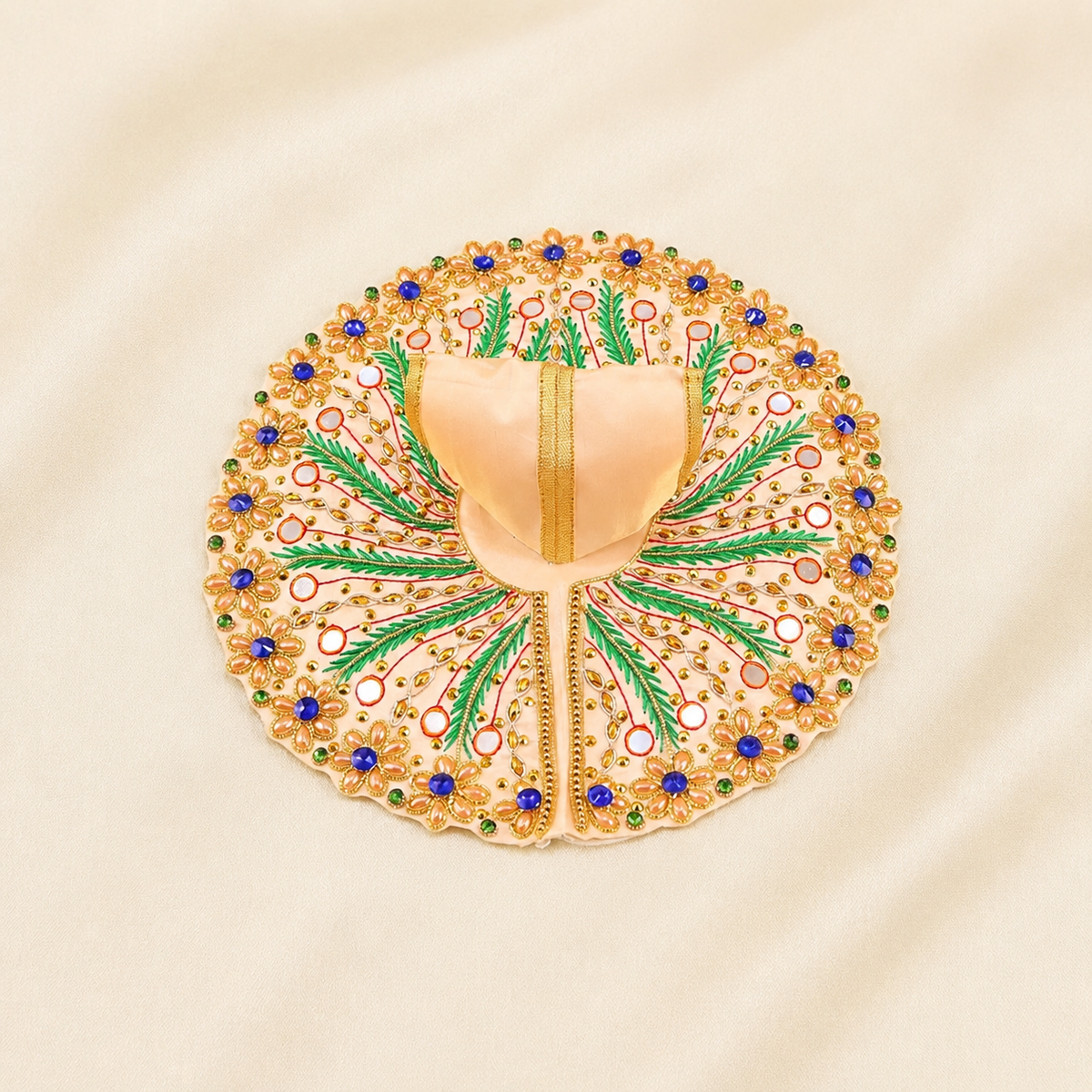 An ornate circular embroidered poshak in peach, gold, green, blue, and white, laid flat on a cream-colored fabric background.