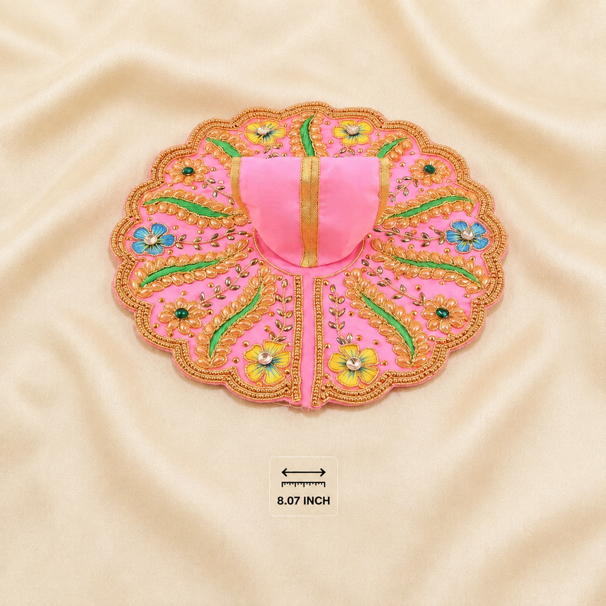A pink embroidered decorative applique or patch with scalloped edges, gold thread detailing, and floral motifs, laid flat on a beige satin fabric background. A small size marker reading 8.
