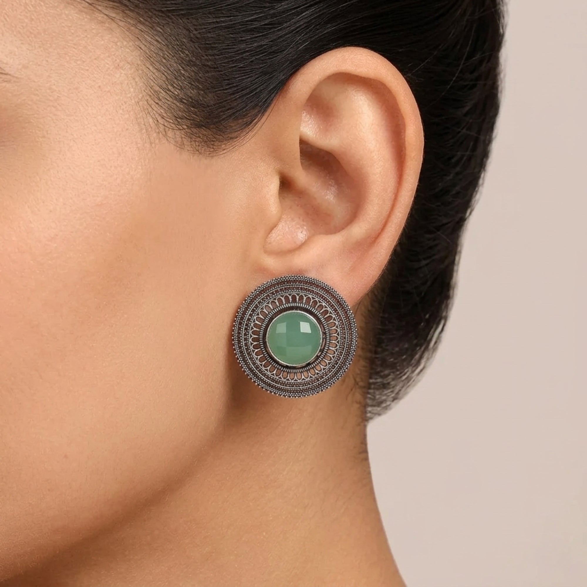 Close-up of an ear wearing a decorative earring with a green gemstone on a neutral background