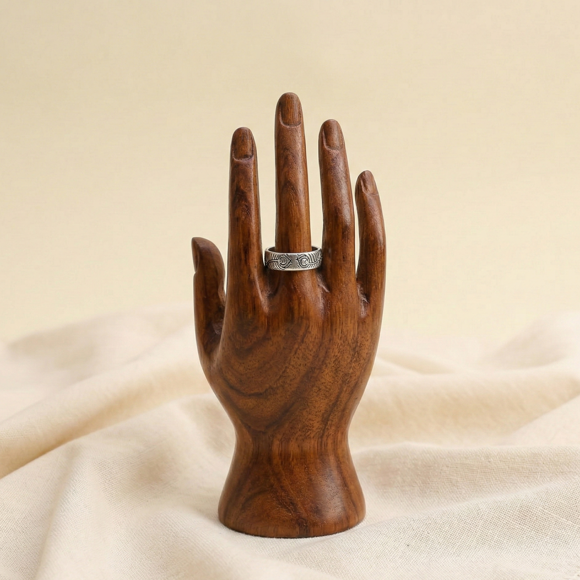 Wooden hand holding a silver ring on a beige fabric background