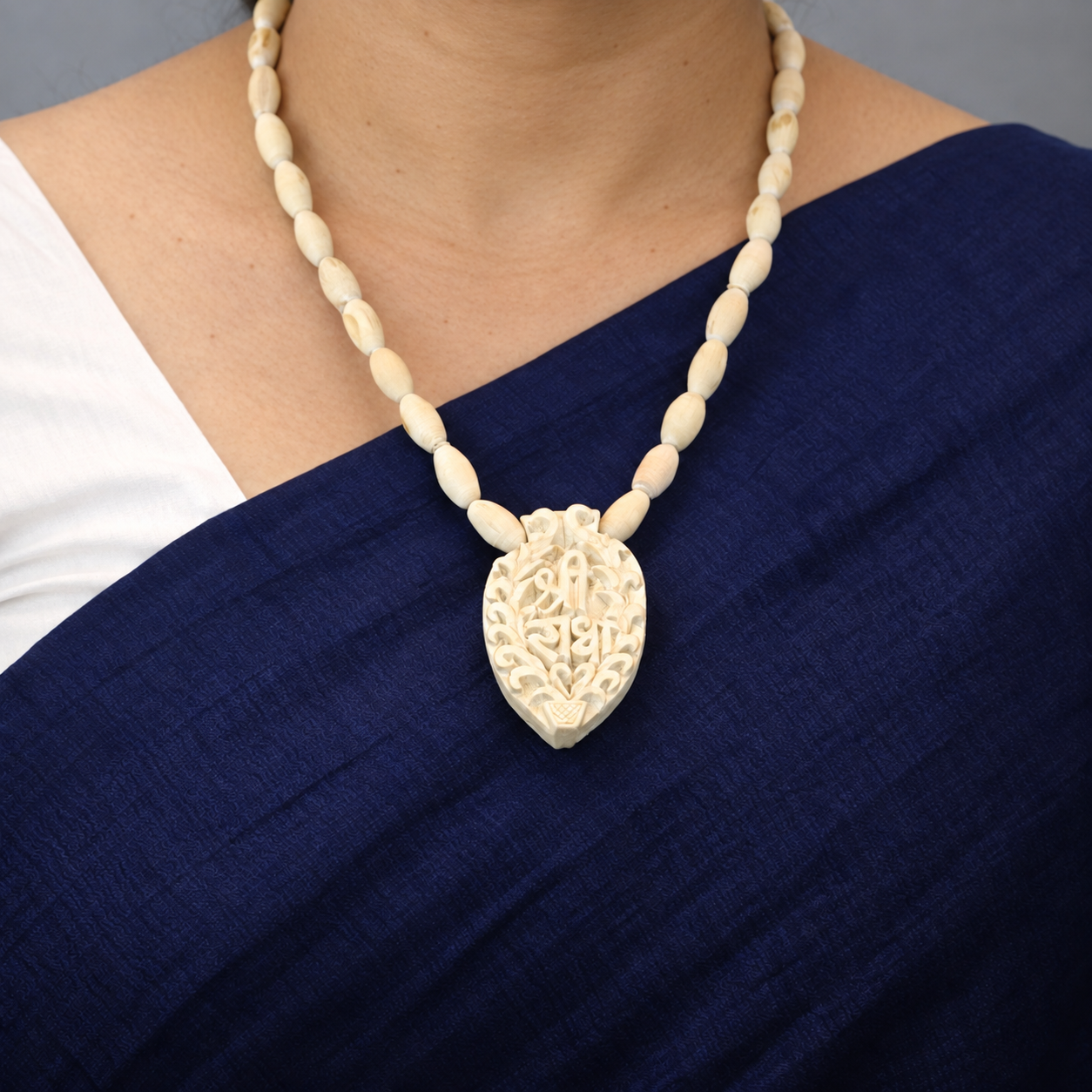 Oval-bead Tulsi mala with a carved leaf-shaped Shri Radha pendant worn with a navy saree.