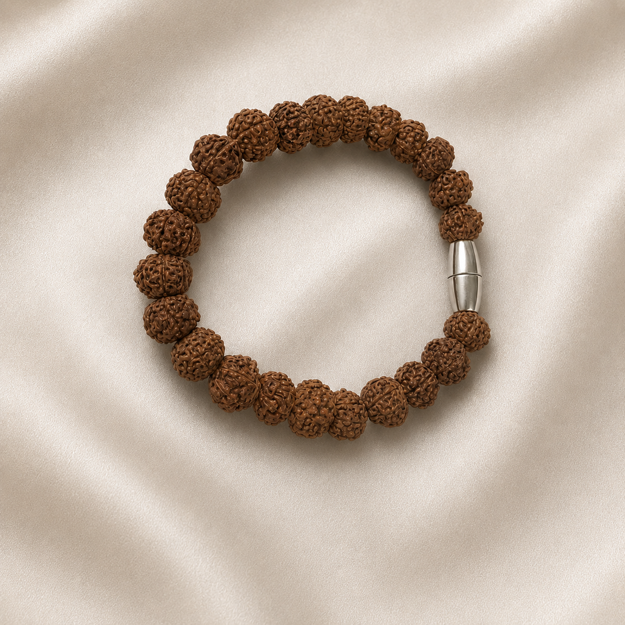 A beaded bracelet made of dark brown textured seed beads with a silver cylindrical clasp, displayed on a cream-colored satin fabric background.