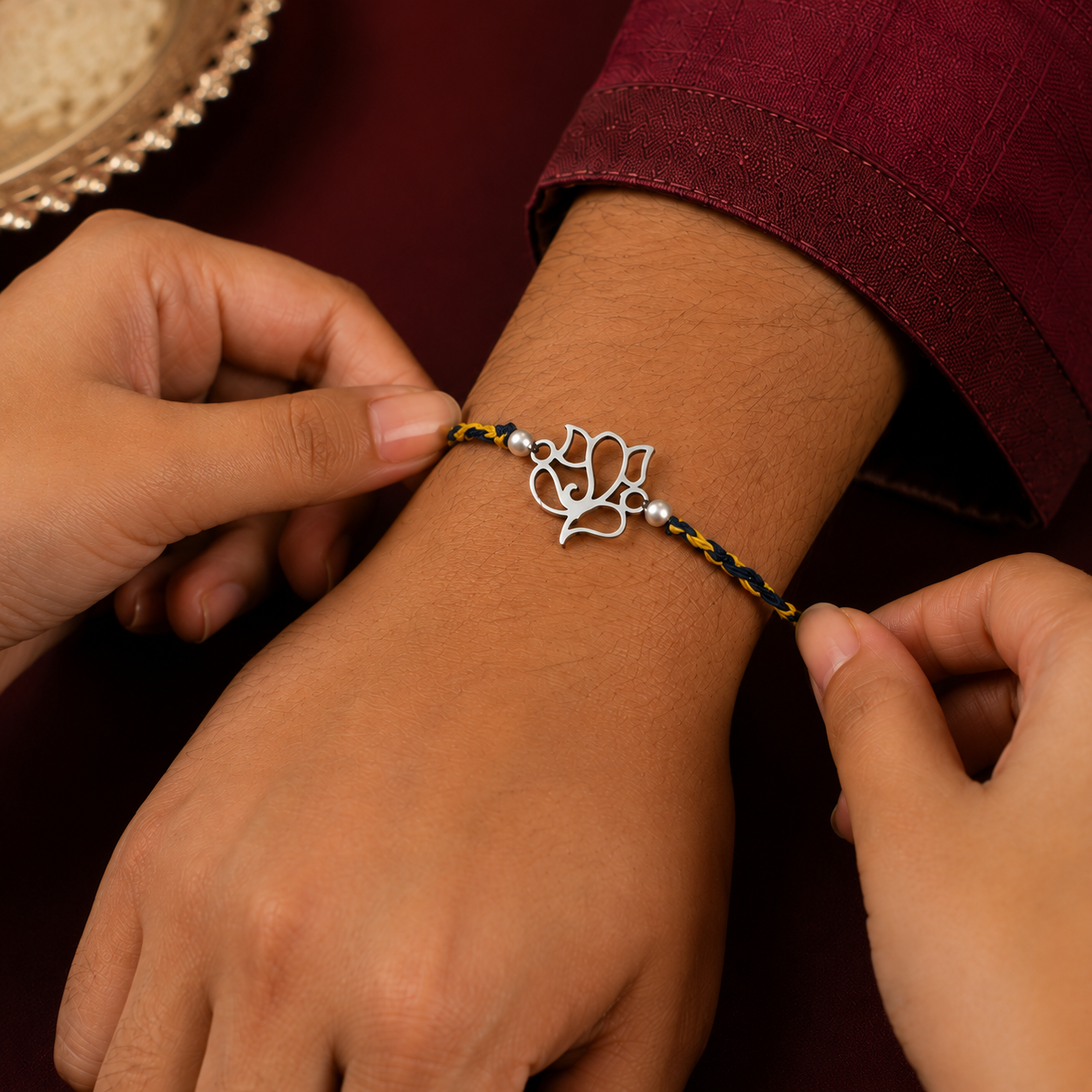 Silver Ganesh Rakhi with yellow-grey braided thread being tied on a wrist