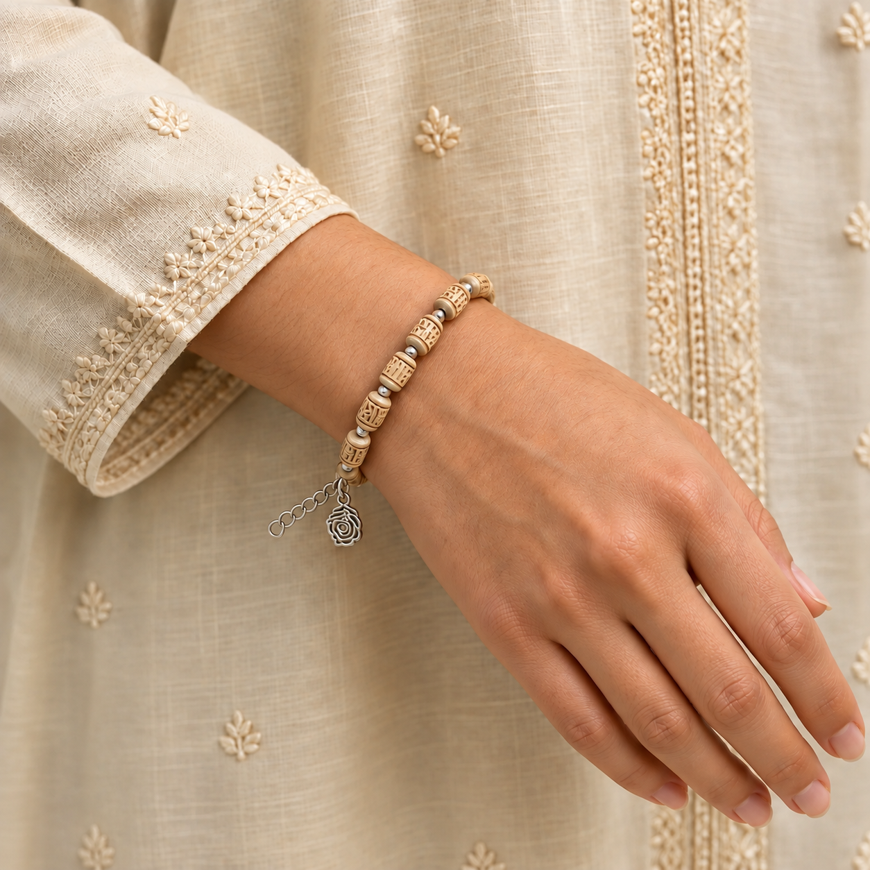 Carved Tulsi bead bracelet with silver-toned spacers, an extension chain and a flower charm worn on a wrist.