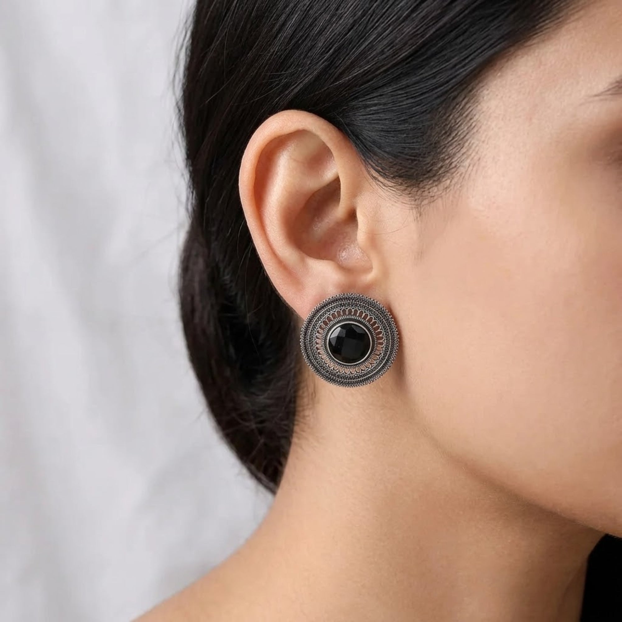 Black oxidized metal stud earring with round stone and intricate filigree design worn by woman