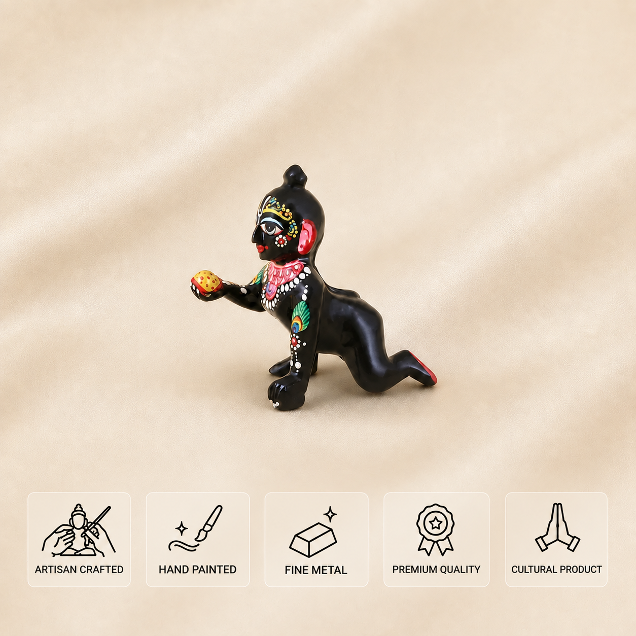 A small black decorative laddu gopal with colorful hand-painted details is shown on a beige fabric background, with five feature icons along the bottom reading Artisan Crafted, Hand Painted, Fine Metal, Premium Quality, and Cultural Product.