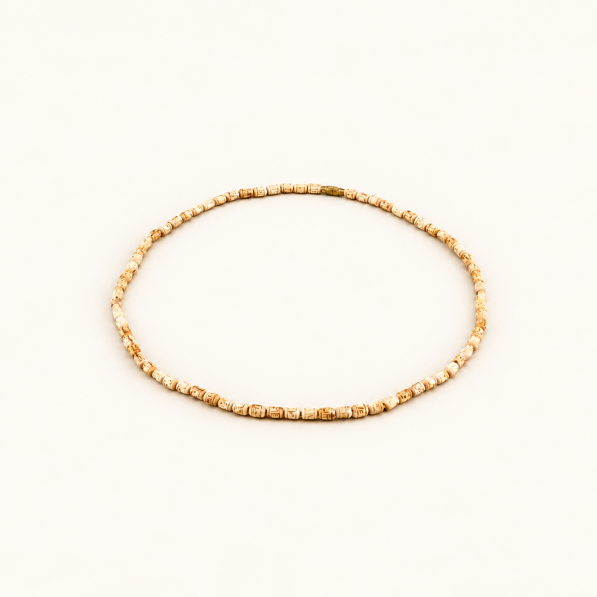 Off-white background par oval shape mein rakhi carved Tulsi bead mala.