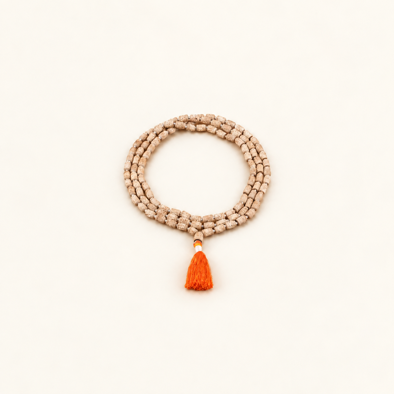 Carved Tulsi japa mala arranged in a coil with an orange tassel on an off-white background.