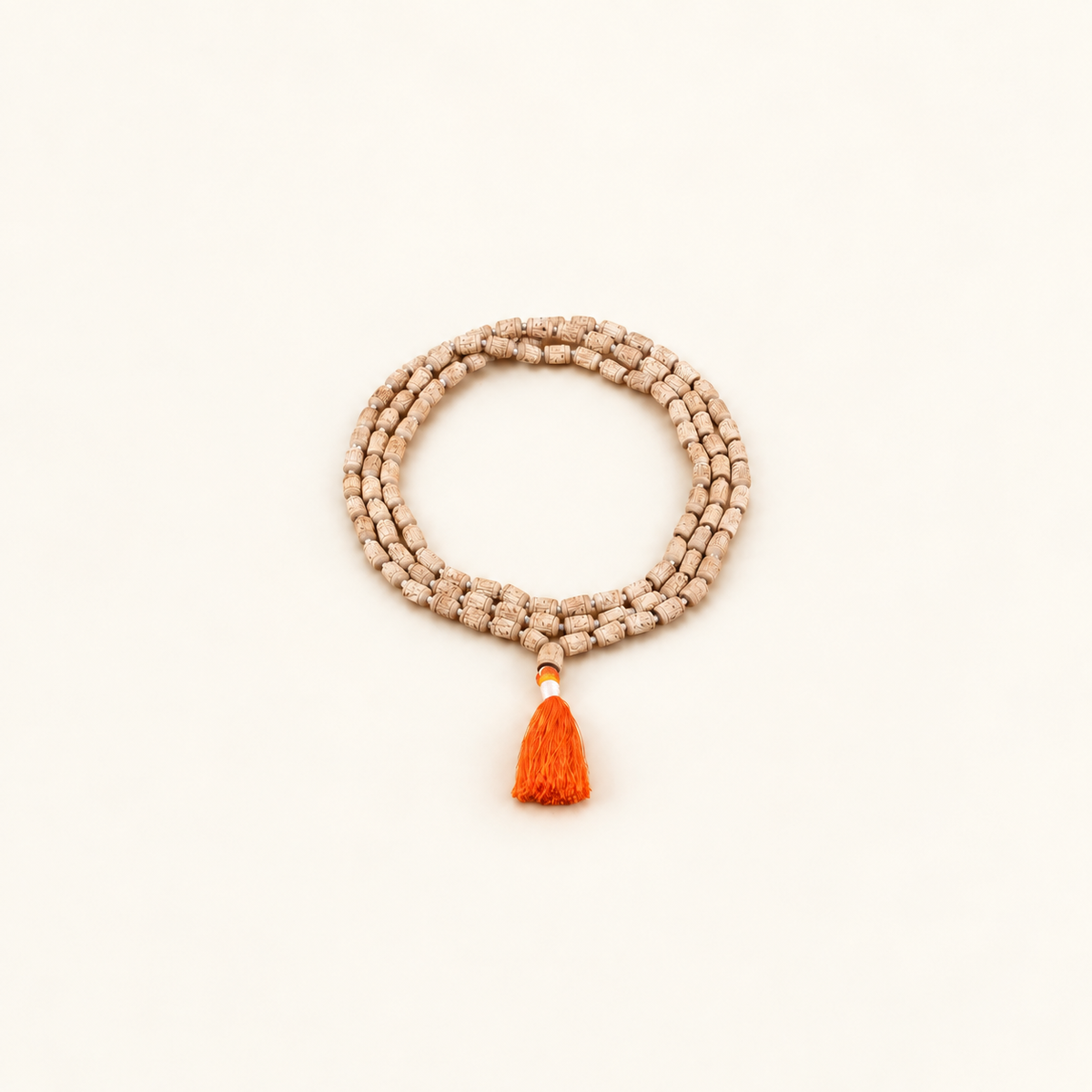 Carved Tulsi japa mala arranged in a coil with an orange tassel on an off-white background.