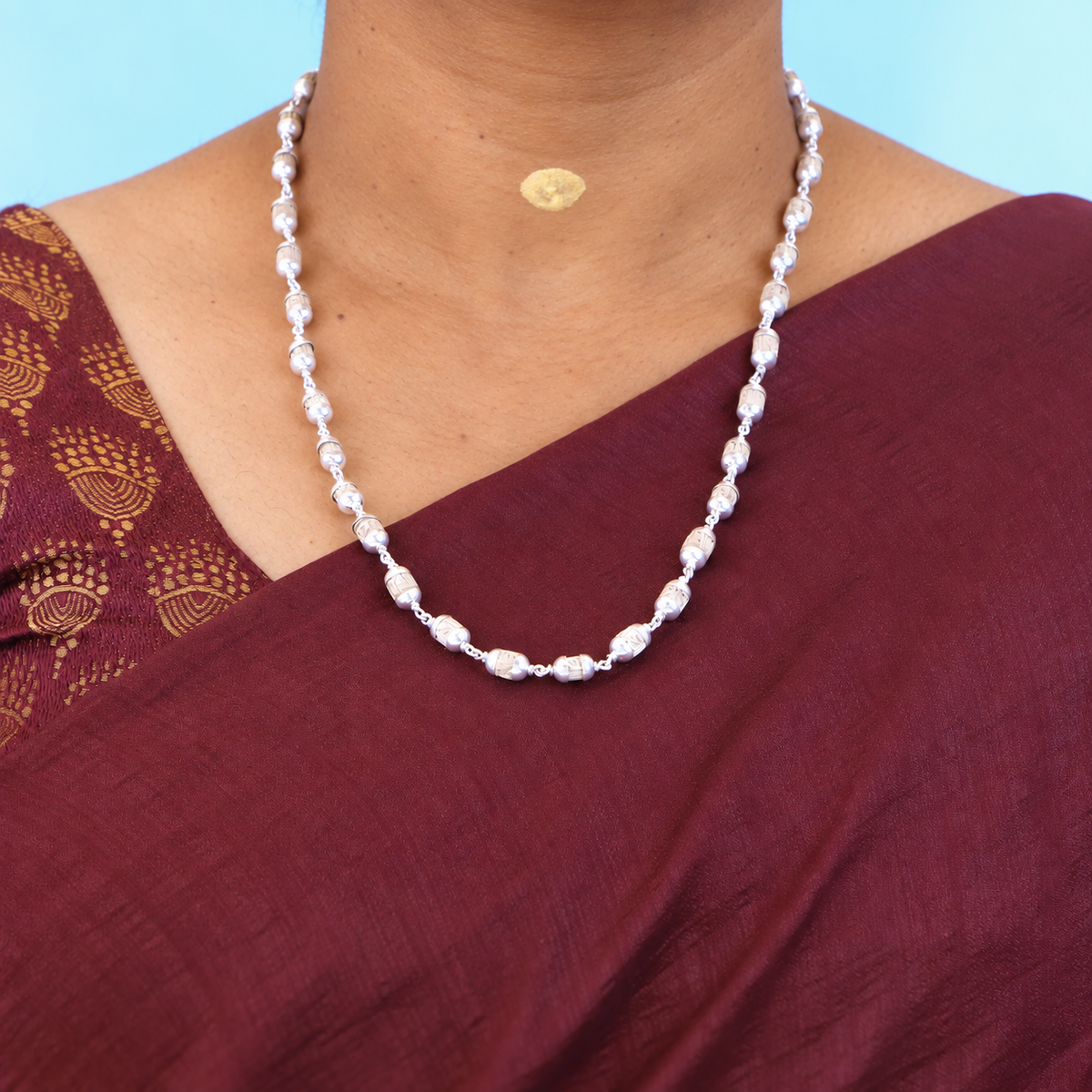 Tulsi mala with carved barrel beads, silver-toned caps and connecting links worn with a maroon saree.