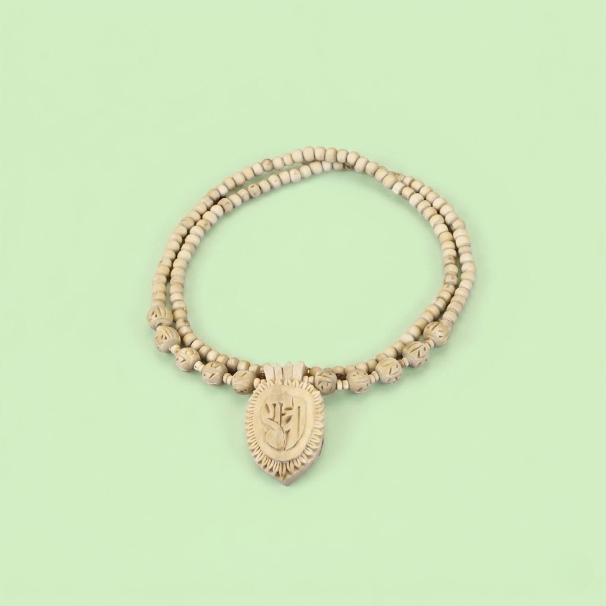 Close up of a hand-carved wooden pendant inscribed with the name Radha on a Tulsi necklace