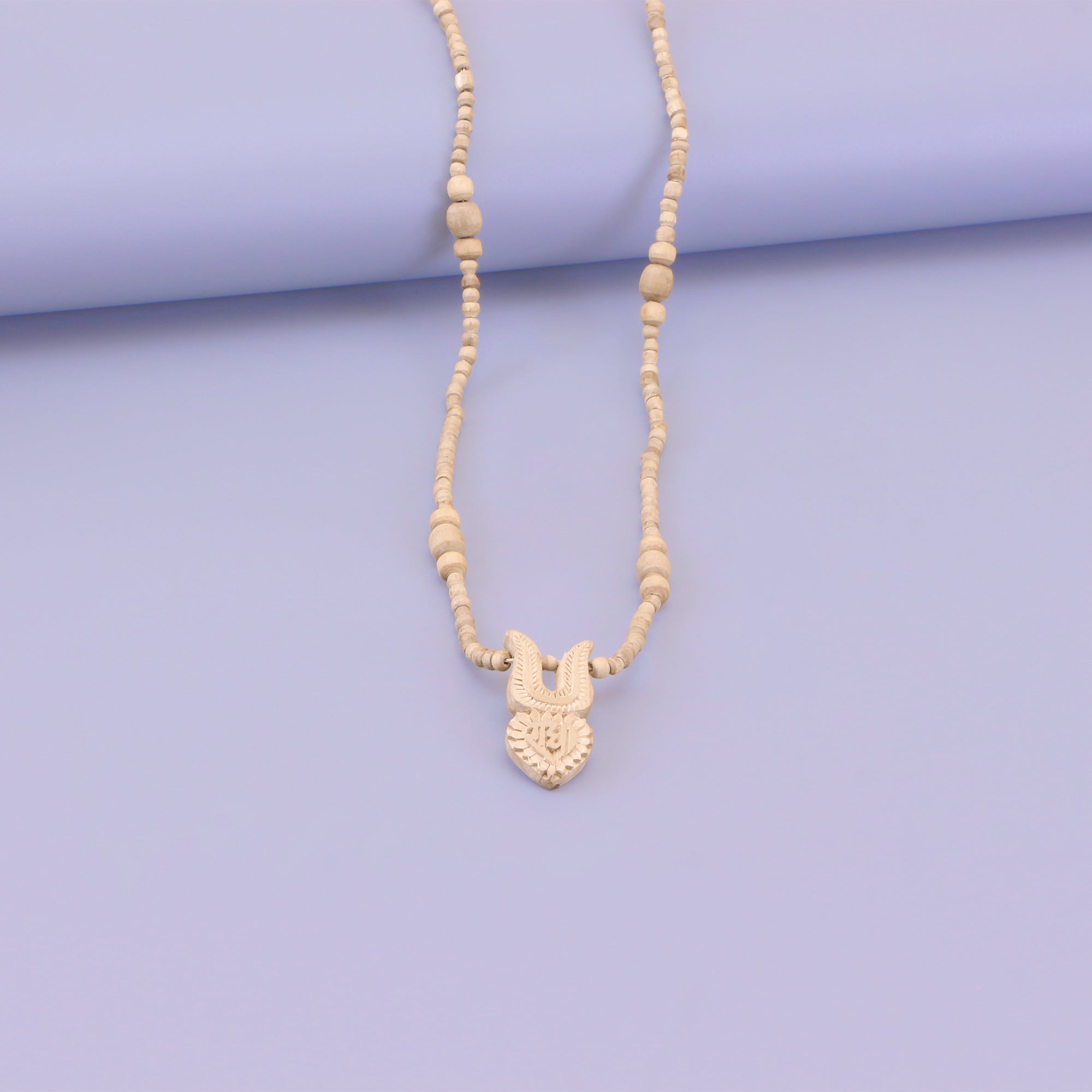 Close up detail of the handmade wooden Shri Radha tilak pendant on a Tulsi bead necklace