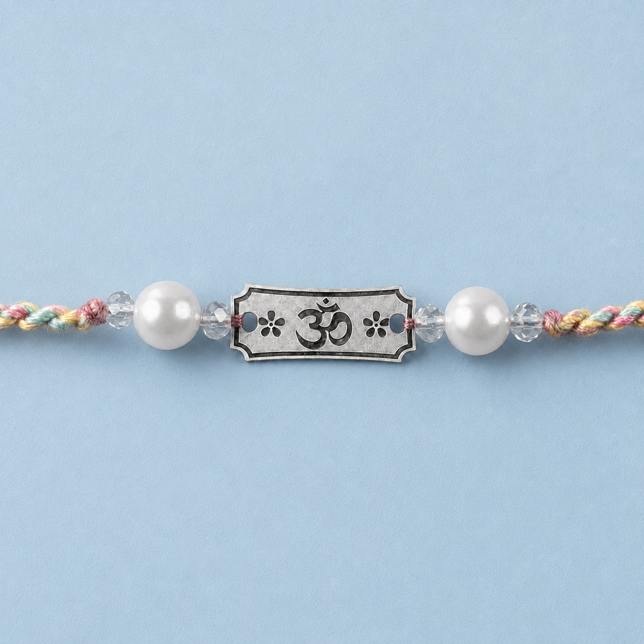 Close up view of engraved 925 sterling silver Om Subh Labh charm with pearl beads on blue silk