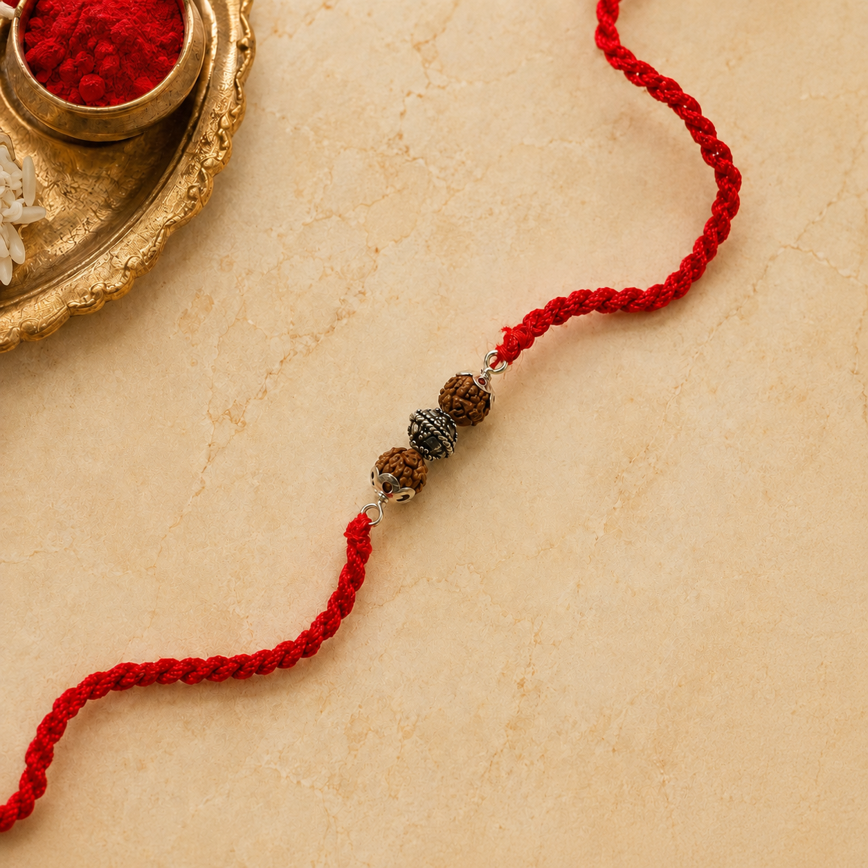 Close up view of sterling silver capped three Rudraksha beads on red thread with puja thali