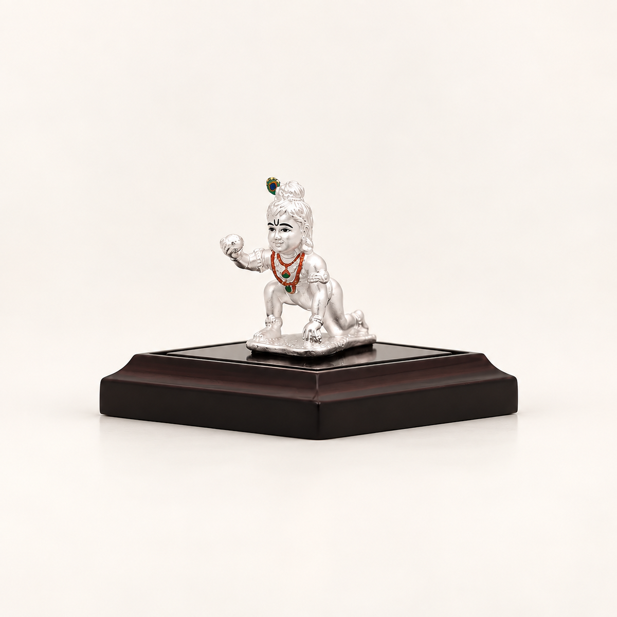 Three-quarter view of a silver crawling Laddu Gopal idol on a dark display stand against an off-white background.