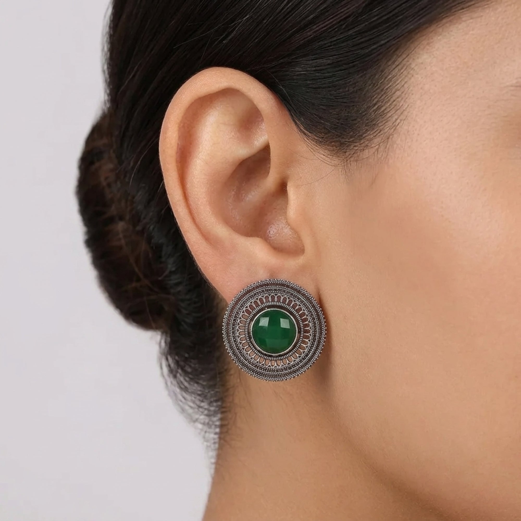 Dark green oxidized metal stud earring with round stone and intricate metal filigree design worn on ear