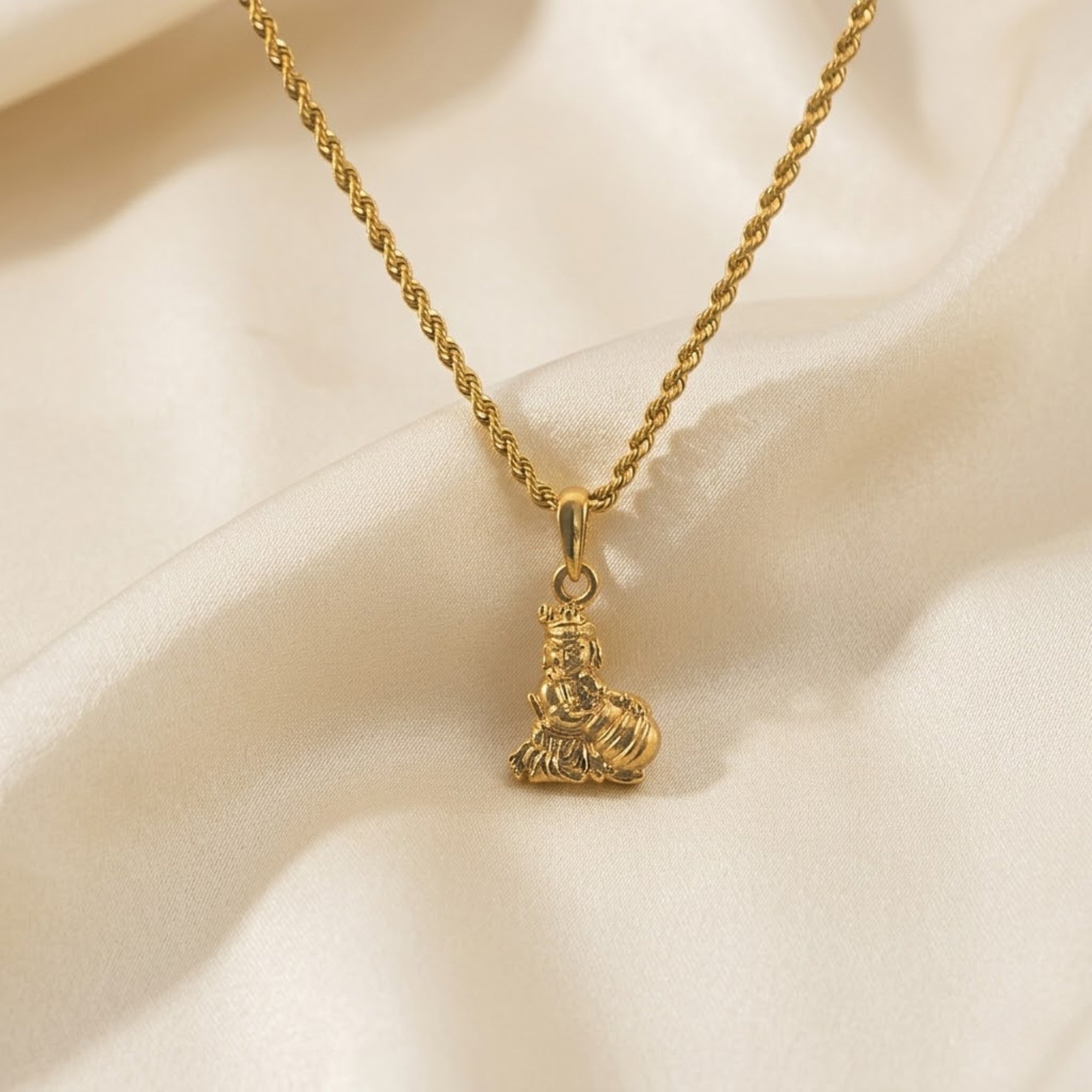 Divine gold Laddu Gopal Krishna figure pendant on gold rope chain displayed on cream silk backdrop