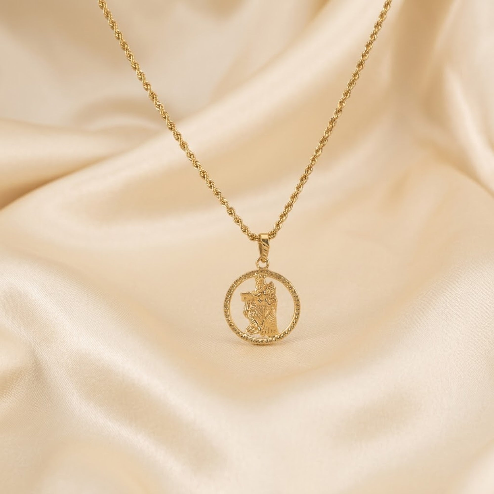 Divine gold Radha Krishna pendant on gold chain displayed on cream silk fabric