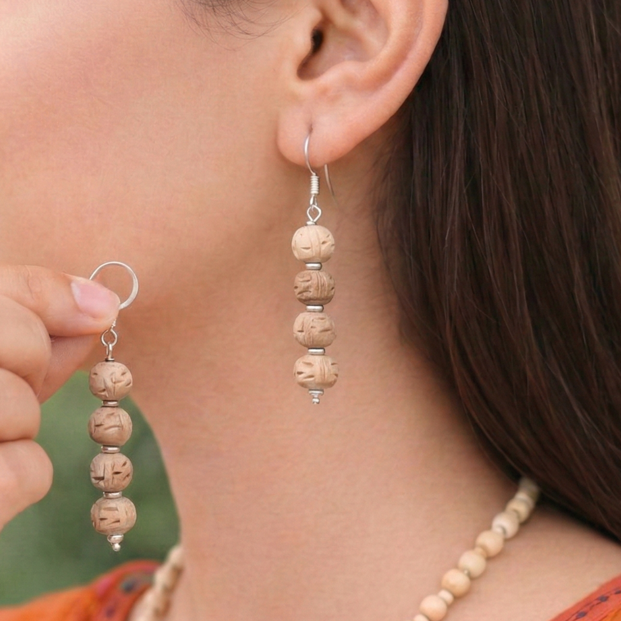 Woman wearing elegant silver dangle earrings featuring carved authentic Tulsi wood beads