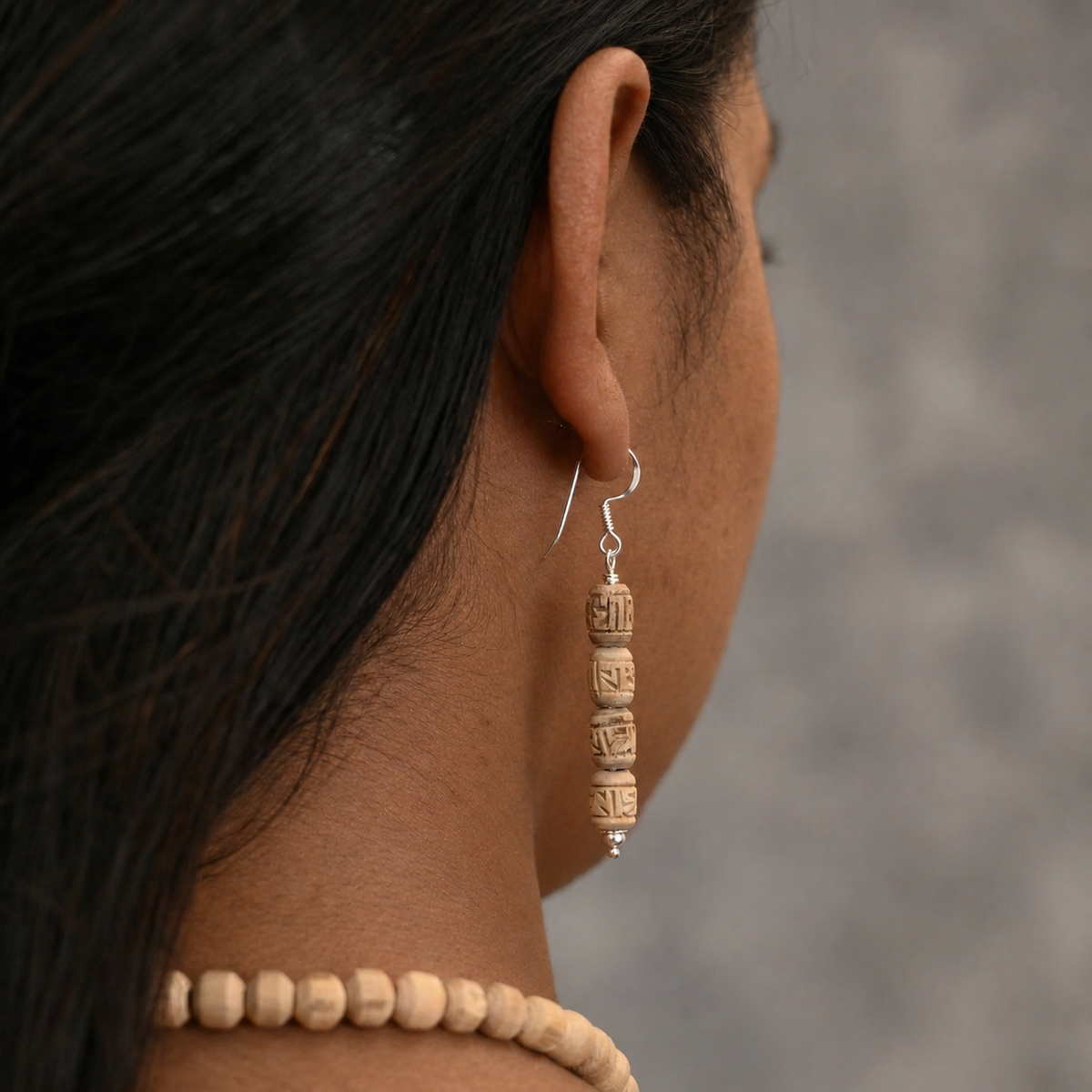 Tulsi drop earring with four carved barrel-shaped wooden beads and a silver-toned hook, viewed from behind the ear.
