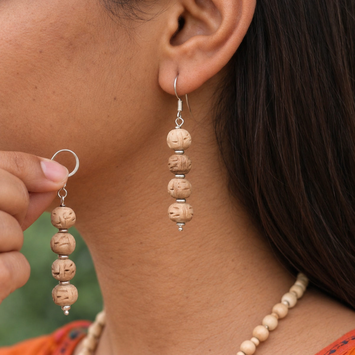Four-bead carved Tulsi drop earrings with silver-toned spacers, one worn and the matching earring held beside it.