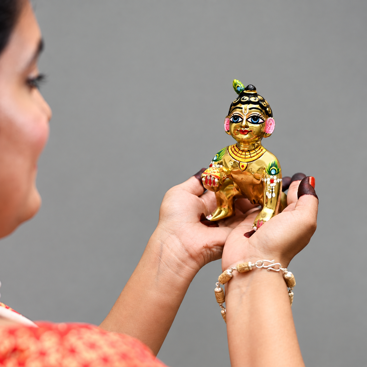 Hand-painted golden Laddu Gopal idol held in hands.