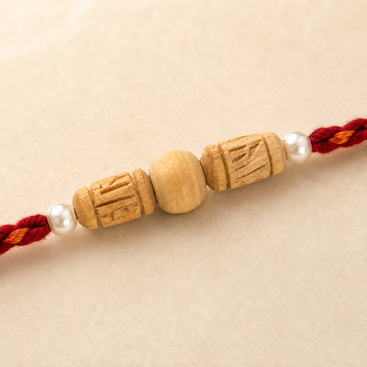 handcrafted Tulsi wood beads flanked by white pearls on a red and orange braided Rakhi thread.