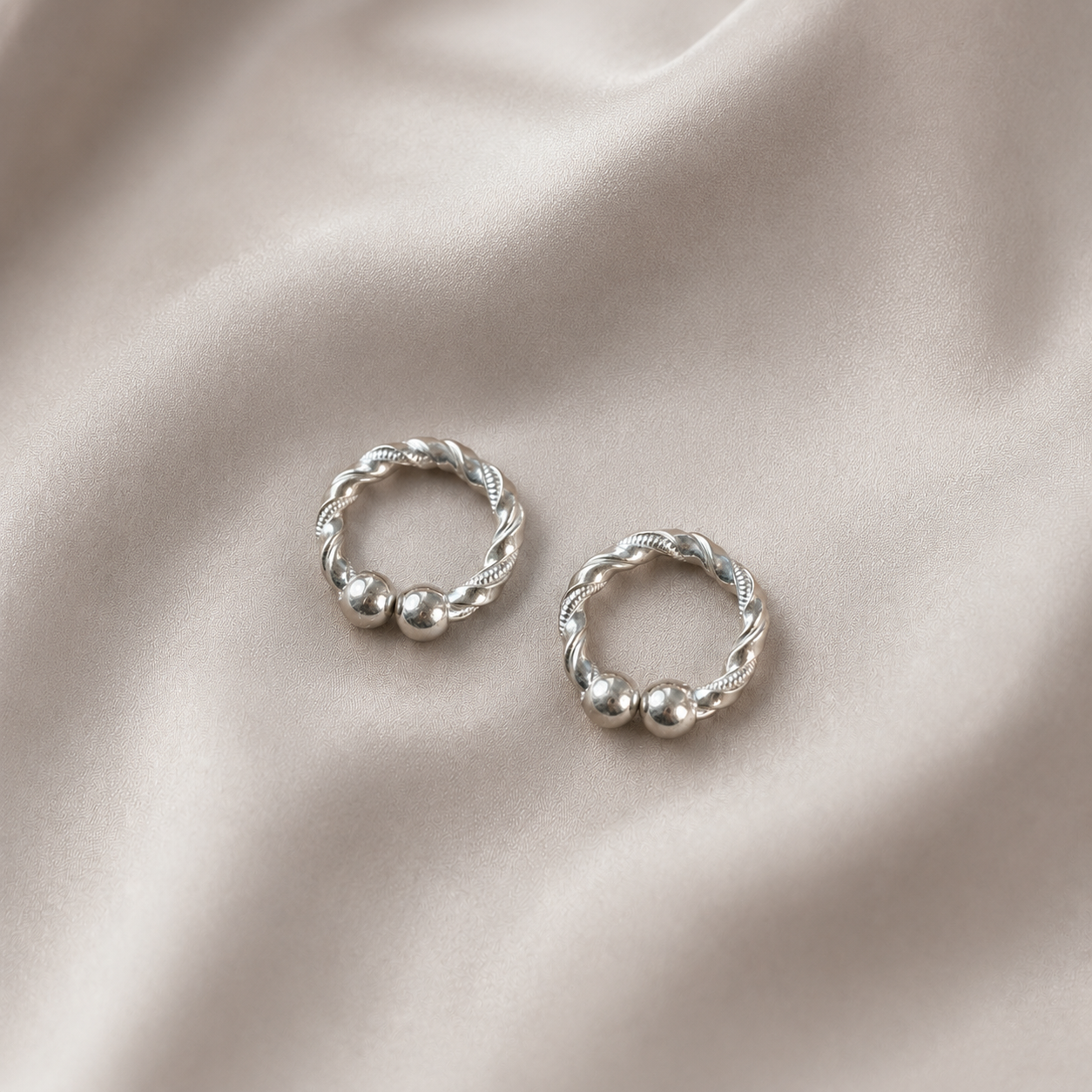 Pair of handcrafted silver kada for Kanha Ji displayed on soft cream silk backdrop