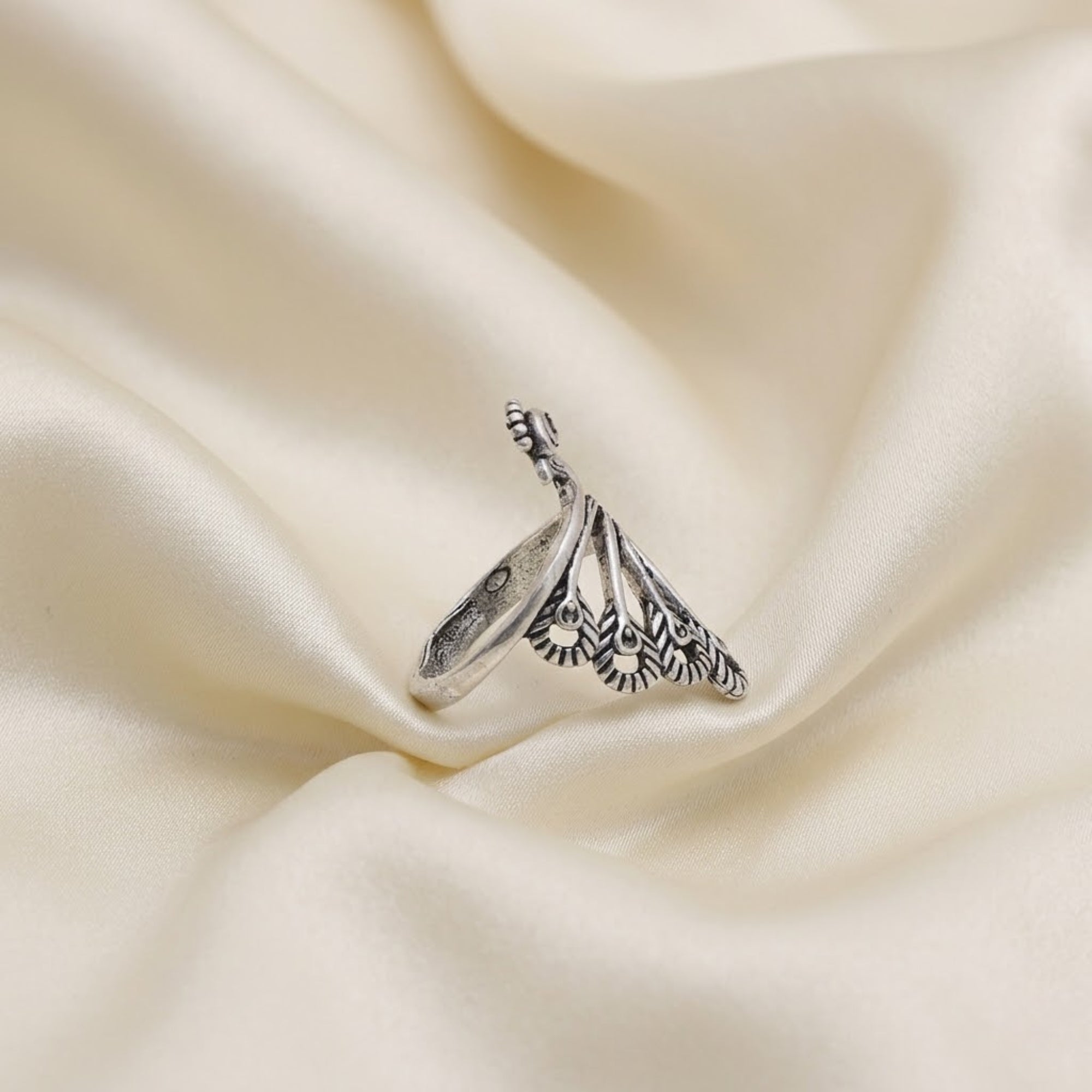 Handmade oxidized metal peacock ring displayed on plain beige background