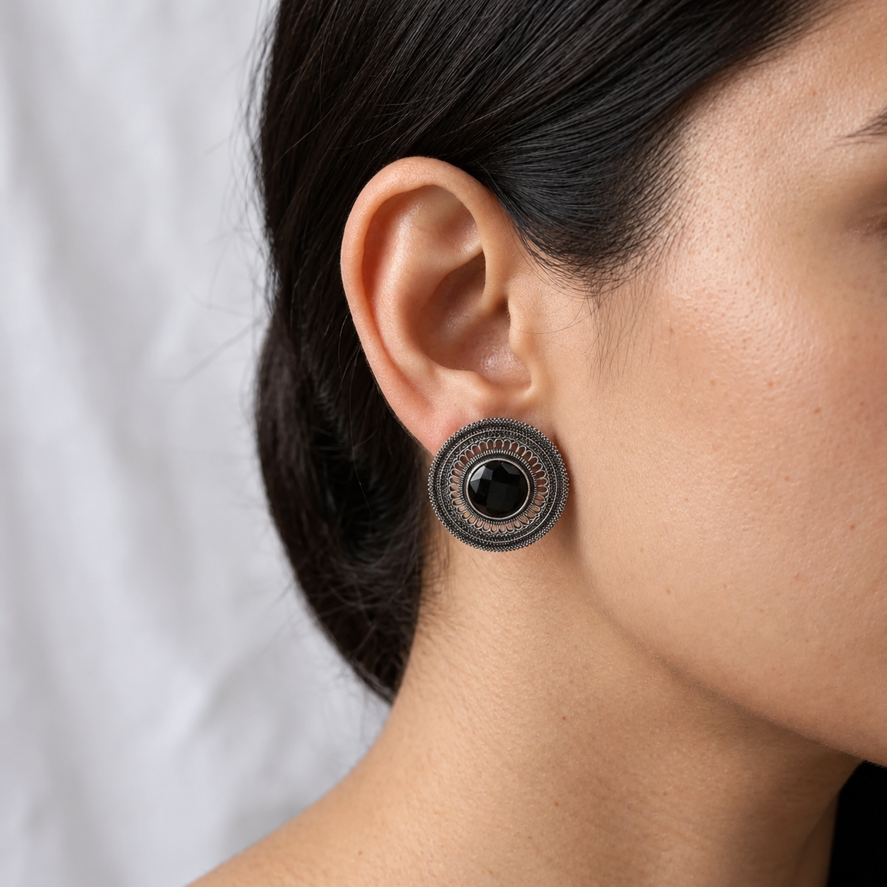 Model wearing a round imitation filigree earring with a black centre stone