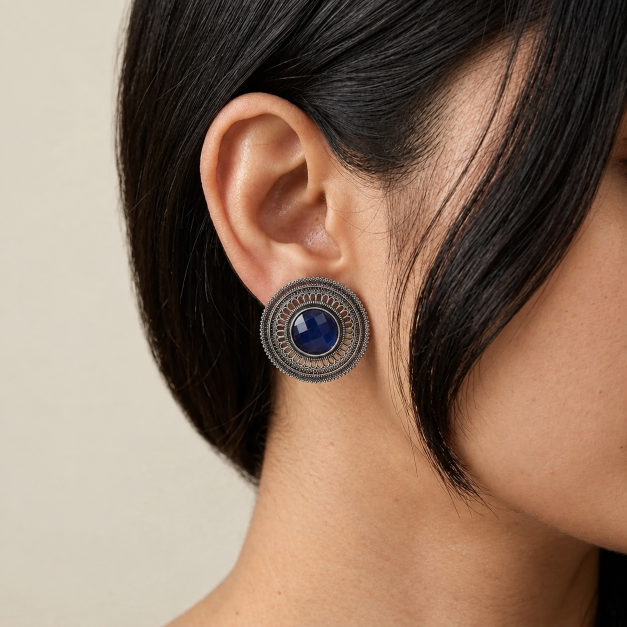 Model wearing a round imitation filigree earring with a deep blue centre stone