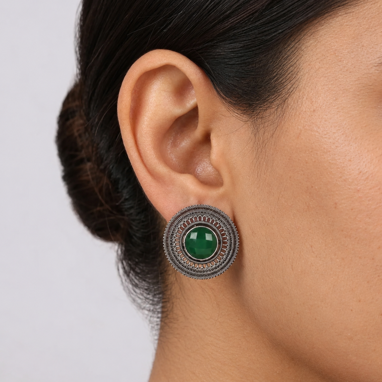 Model wearing a round imitation filigree earring with a deep green centre stone