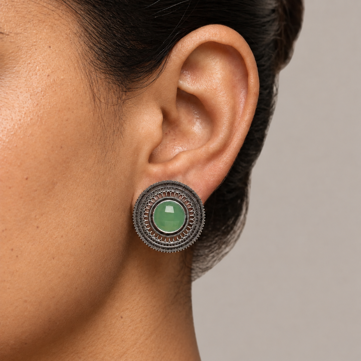 Model wearing a round imitation filigree earring with a light green centre stone
