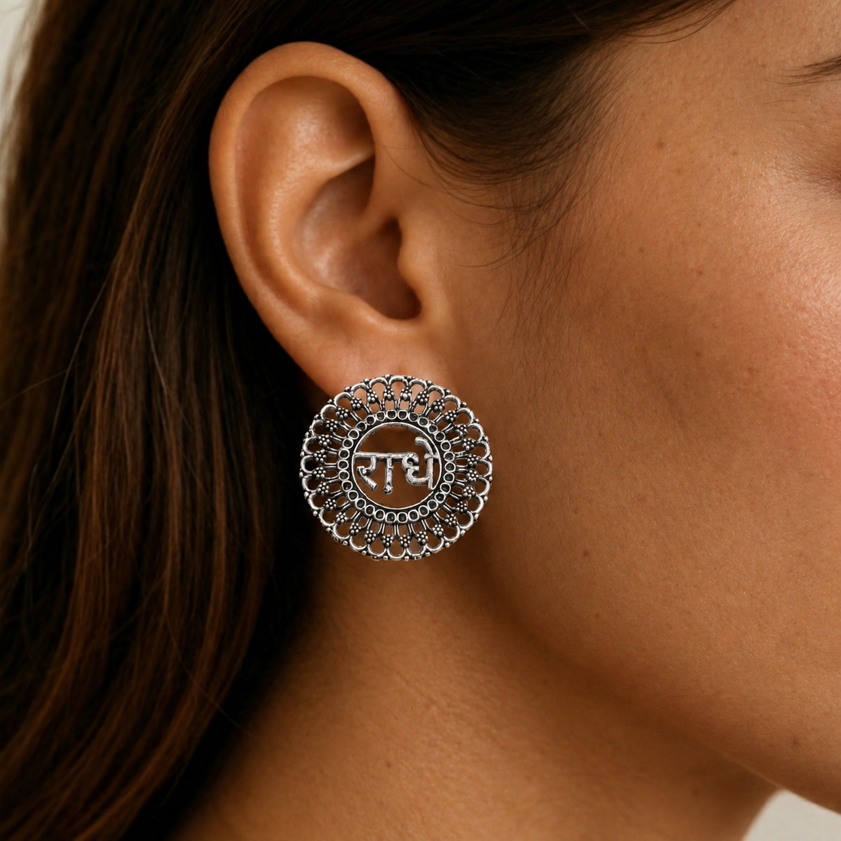 A round imitation earring with an oxidised silver-tone filigree design and central Devanagari devotional motif