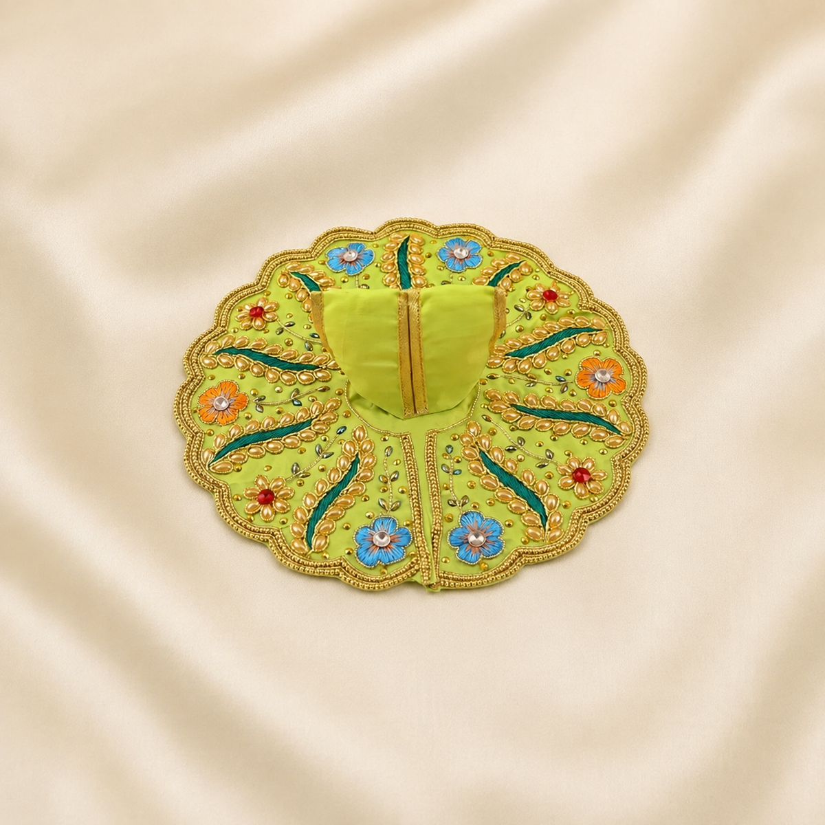 A circular embroidered poshakin light green, featuring a central stitched panel and a scalloped border with blue, orange, red, and teal floral and leaf motifs, displayed on a cream satin fabric background.
