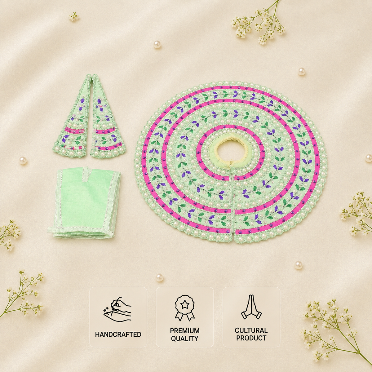 A flat-lay product photograph of a traditional embroidered poshak set on a beige fabric background with decorative pearl beads and baby's breath flowers. The set includes a round poshak with intricate green, pink, and purple floral embroidery, a matching pointed neck warmer, and a folded cloth pouch.