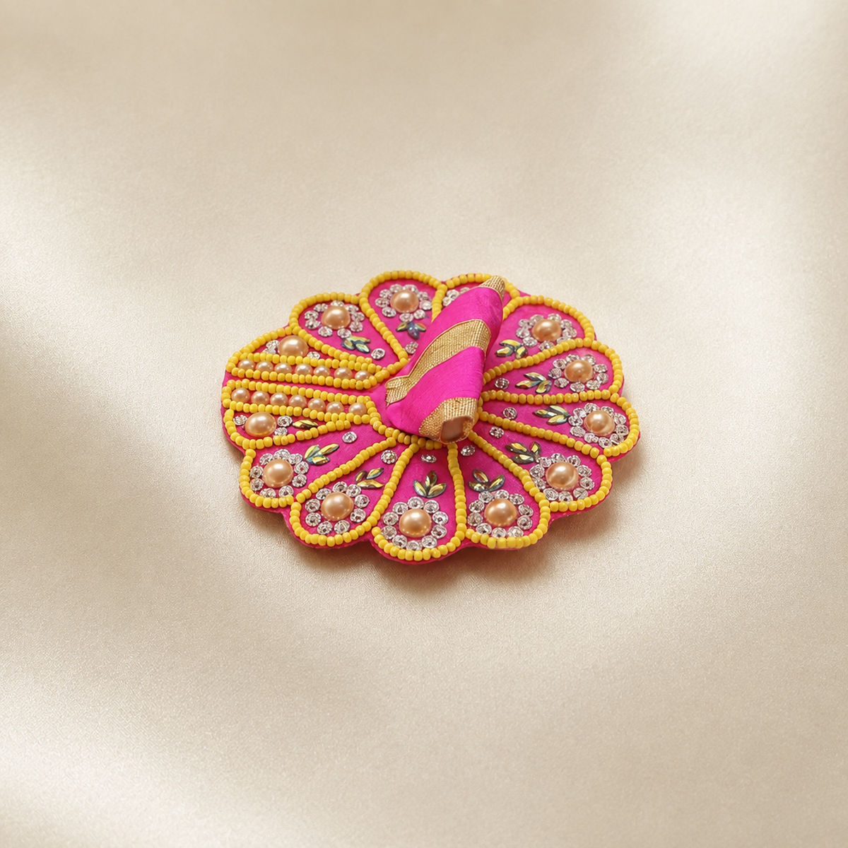 Pink Laddu Gopal dress with yellow beadwork, pearl embellishments, floral stones and gold trim on an ivory satin background.