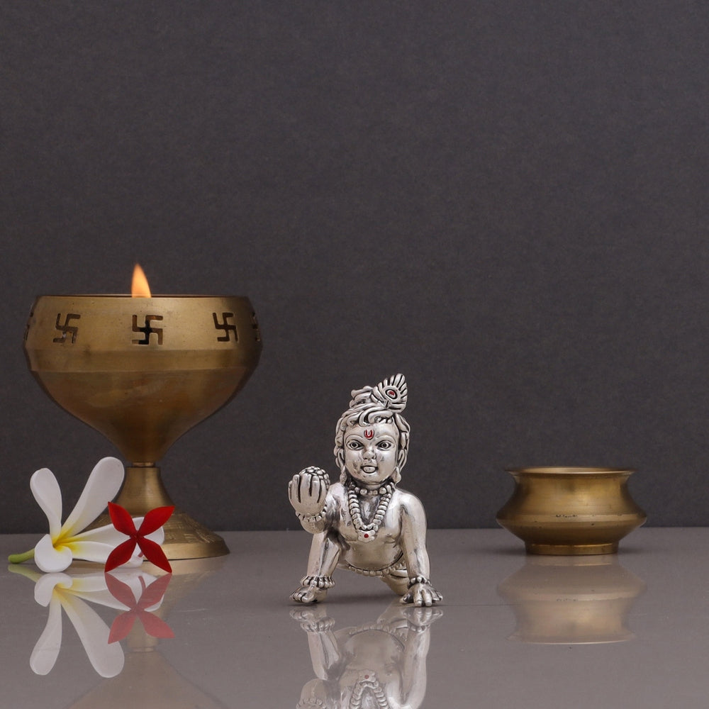 pure silver Laddu Gopal idol of small Kanha Ji displayed with a brass diya
