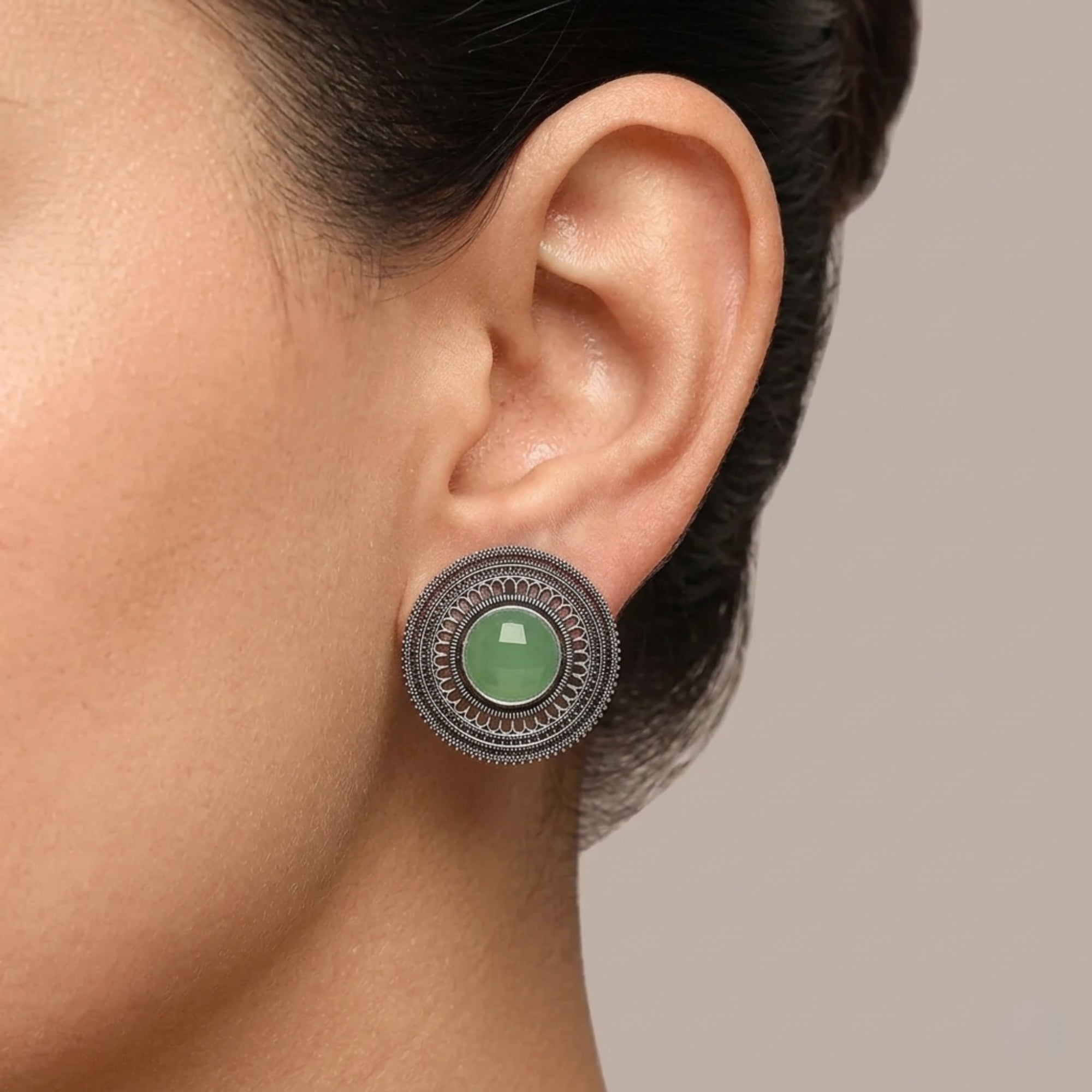 Light green oxidized metal stud earring with intricate round filigree design worn on ear